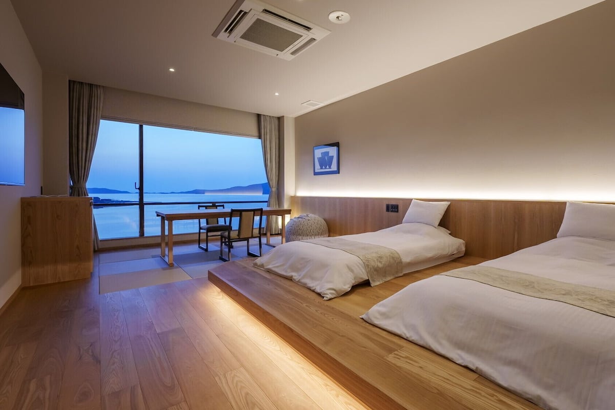 A hotel room with two beds, a desk, and a large window with a view.
