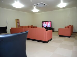 A modern living room with orange sofas, a flat-screen TV, and a ceiling light fixture. - Shimonoseki Station Hotel (Shimonoseki)