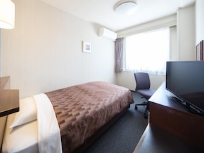 Et hotelværelse med seng, skrivebord med computer, fjernsyn og et vindue med gardiner.