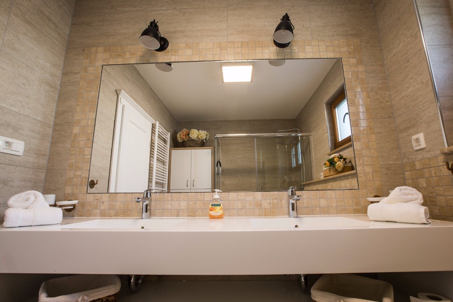 A bathroom with a large mirror, two sinks, a shower, and a towel rack.
