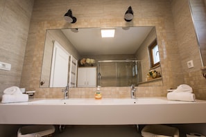 A bathroom with a large mirror, two sinks, a shower, and a towel rack.