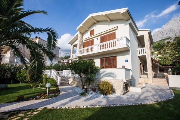 A two-story house with a balcony, a stone staircase, and a well-maintained garden.