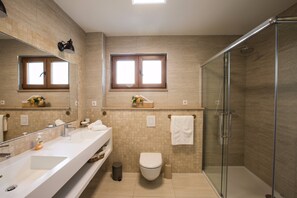 A modern bathroom with a glass-enclosed shower, a large mirror, and two windows.