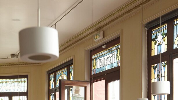 A restaurant interior with wooden tables and benches, large stained glass windows, and a view of the street outside. - Hidden Bay Hotel (Cayeux-sur-Mer)