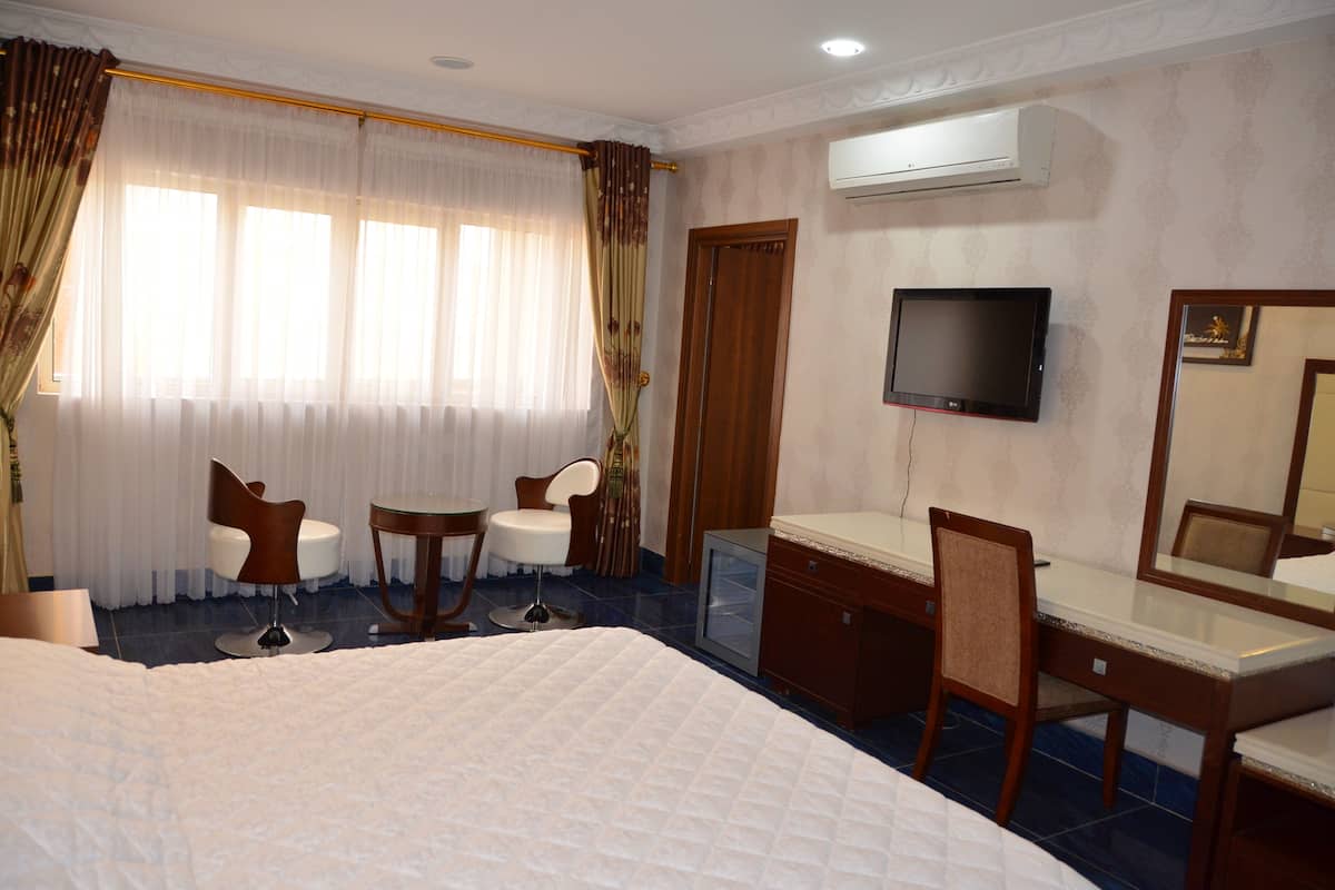 Ein Hotelzimmer mit Bett, Schreibtisch, Stuhl, Fernseher und einem Fenster mit Vorhängen.