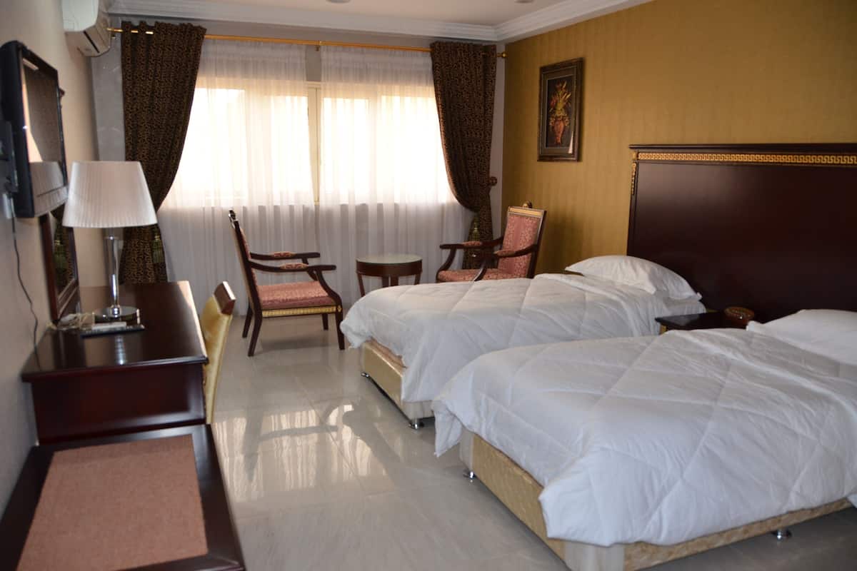 Ein Hotelzimmer mit zwei Betten, einem Schreibtisch mit Lampe, einem Stuhl und einem kleinen Tisch.