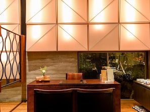 A reception desk with a wooden finish, a vase with flowers, and a menu stand. - Kawatana Onsen Kotengu Sanroji (Shimonoseki)