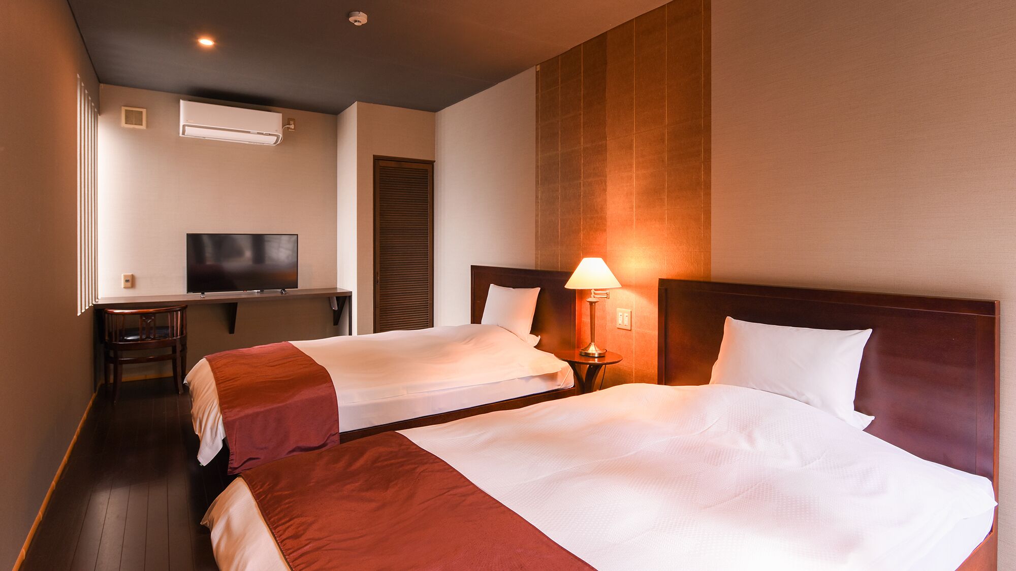 Een hotelkamer met twee bedden, een televisie, een bureau en een lamp.