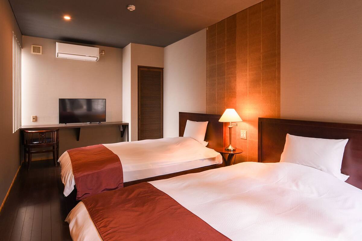 Una habitación de hotel con dos camas, televisión, escritorio y lámpara.