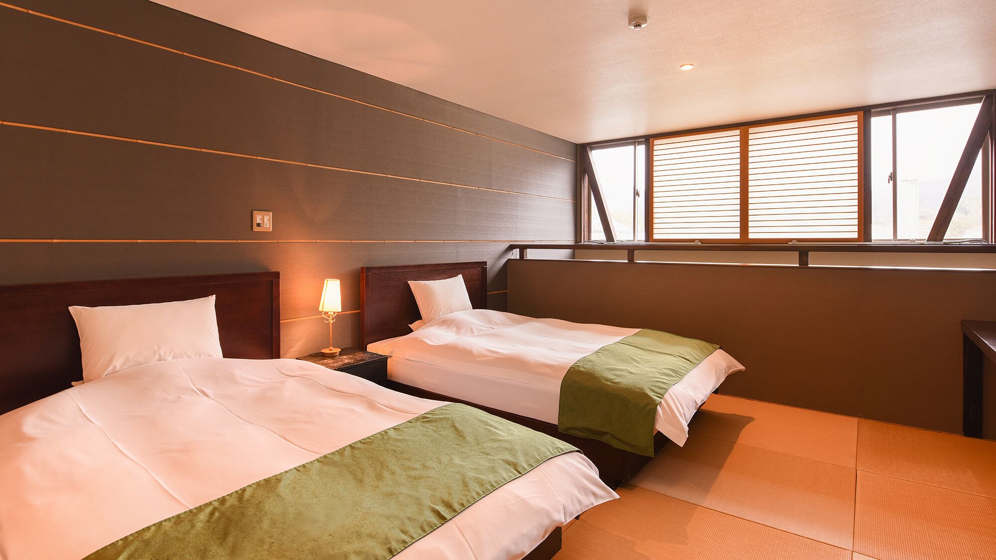 Een hotelkamer met twee bedden, een nachtkastje, een lamp en een raam met jaloezieën.