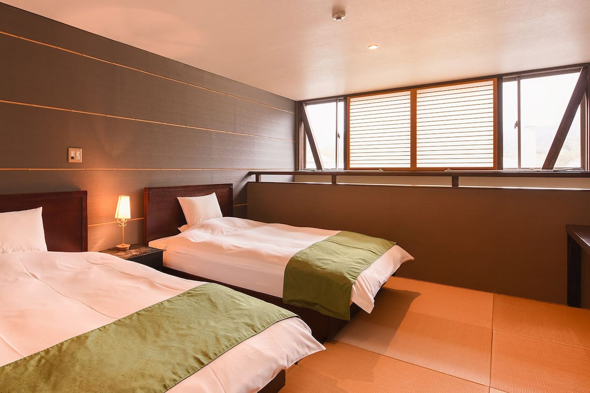 Una habitación de hotel con dos camas, una mesita de noche, una lámpara y una ventana con persianas.