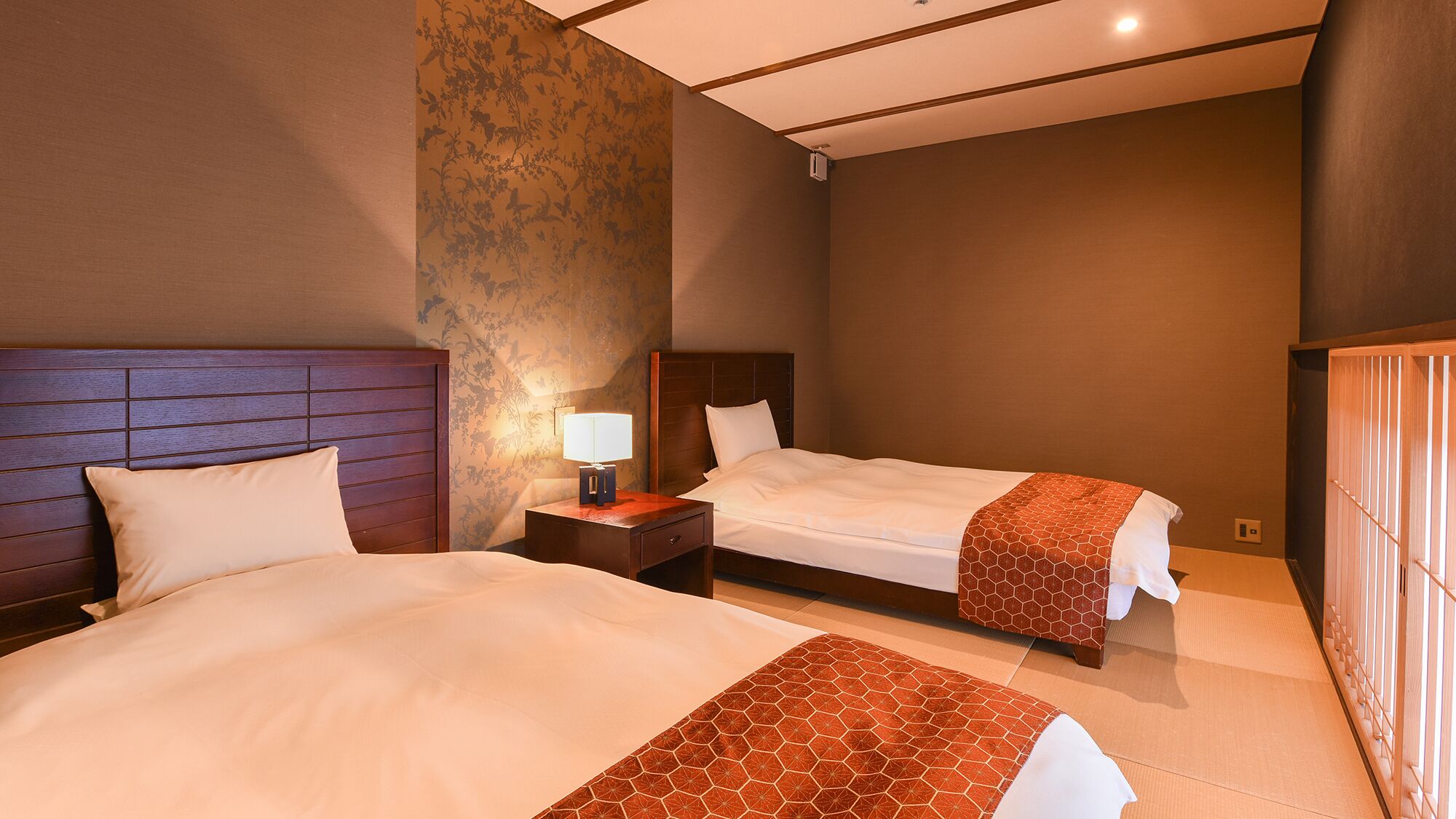 Een hotelkamer met twee bedden, een nachtkastje met een lamp en een groot raam.