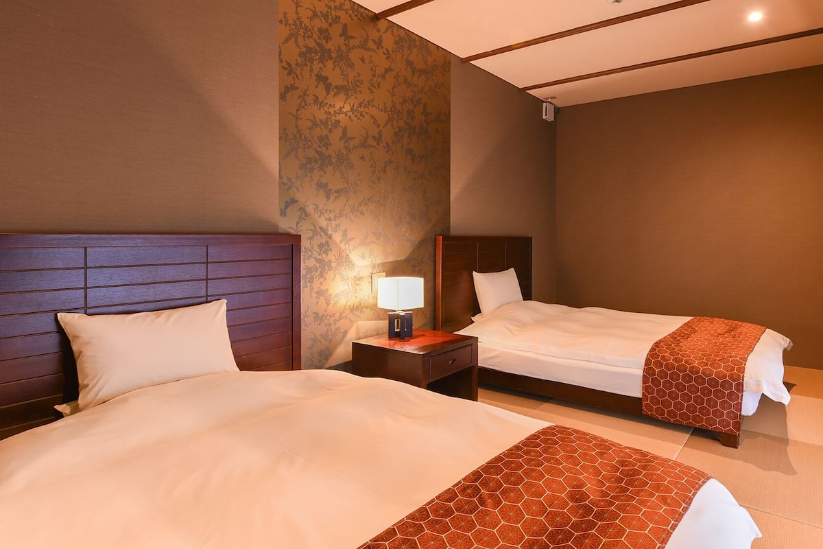 Una habitación de hotel con dos camas, una mesita de noche con lámpara y un ventanal grande.