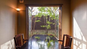 Un espace repas avec une longue table et des chaises, une fenêtre donnant sur les arbres et une lampe fixée au mur.
