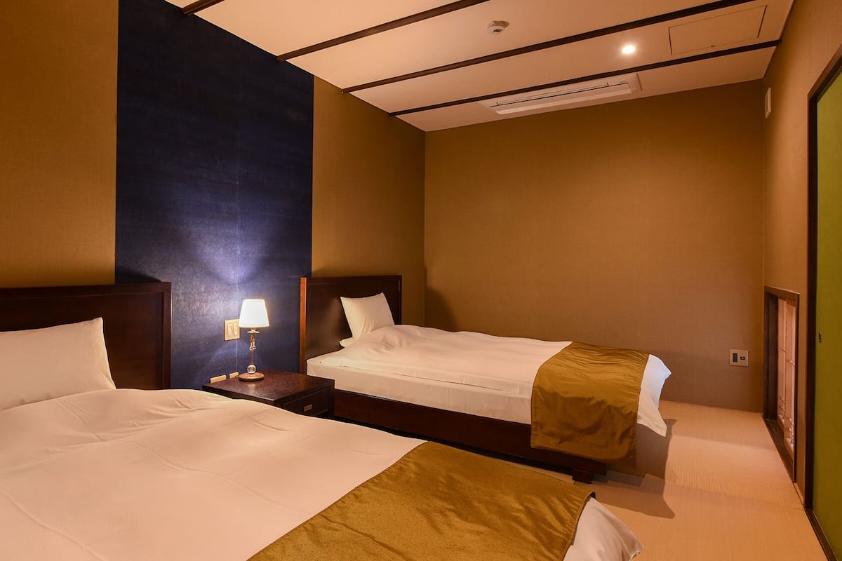 Habitación de hotel con dos camas, una mesita de noche con lámpara e iluminación empotrada en el techo.
