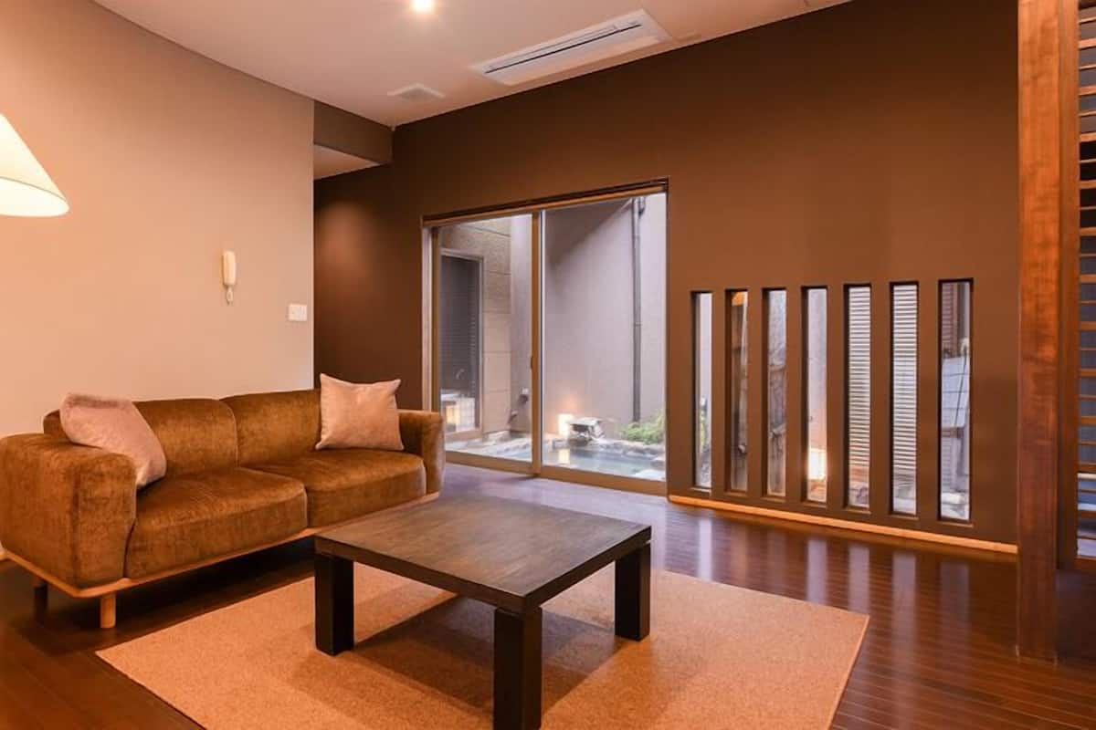 Una sala de estar moderna con un sofá, una mesa de centro, una lámpara y un ventanal corredizo que da a un espacio exterior.