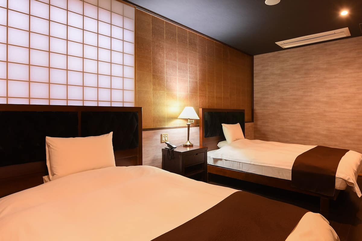 Una habitación de hotel con dos camas, una mesita de noche con lámpara y un ventanal con diseño de cuadrícula.