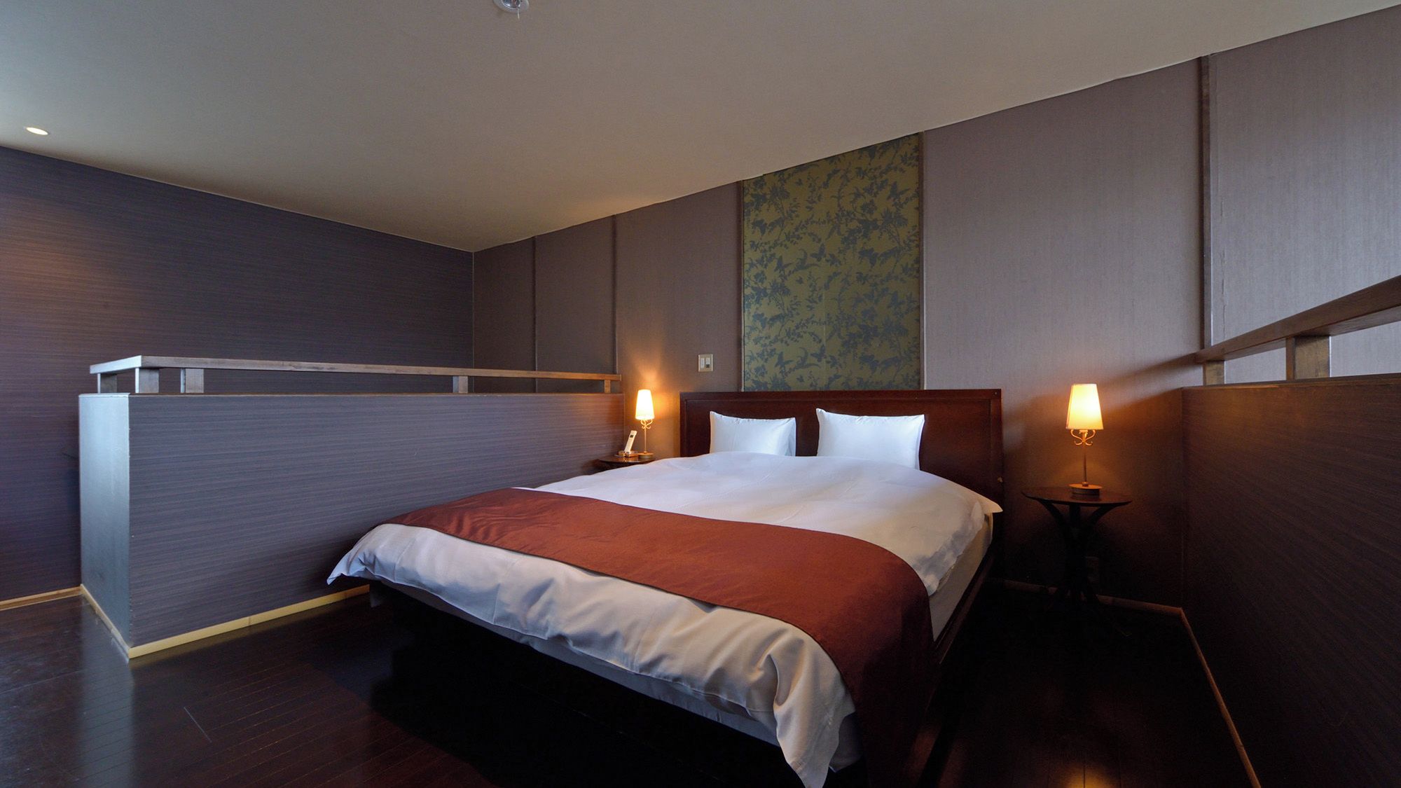Una habitación de hotel con una cama grande, dos lámparas de noche, un cabecero de madera y un papel tapiz estampado en la pared.