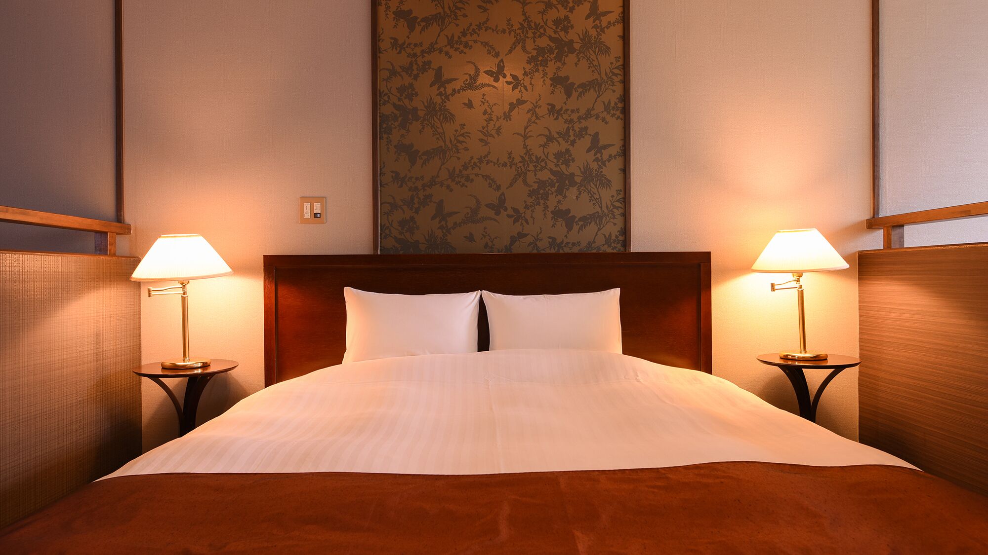 Een hotelkamer met een groot bed, twee bedlampen, een houten hoofdeinde en bloemenbehang.