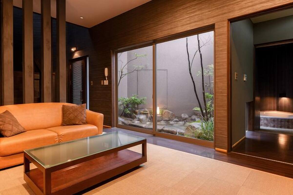Una sala de estar moderna con un sofá, una mesa de centro de vidrio y vistas a un paisaje natural a través de amplios ventanales correderas.