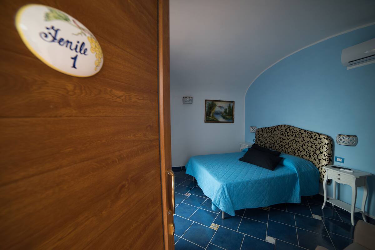 A bedroom with a bed, a nightstand, a wall-mounted air conditioner, and a door with a plaque.