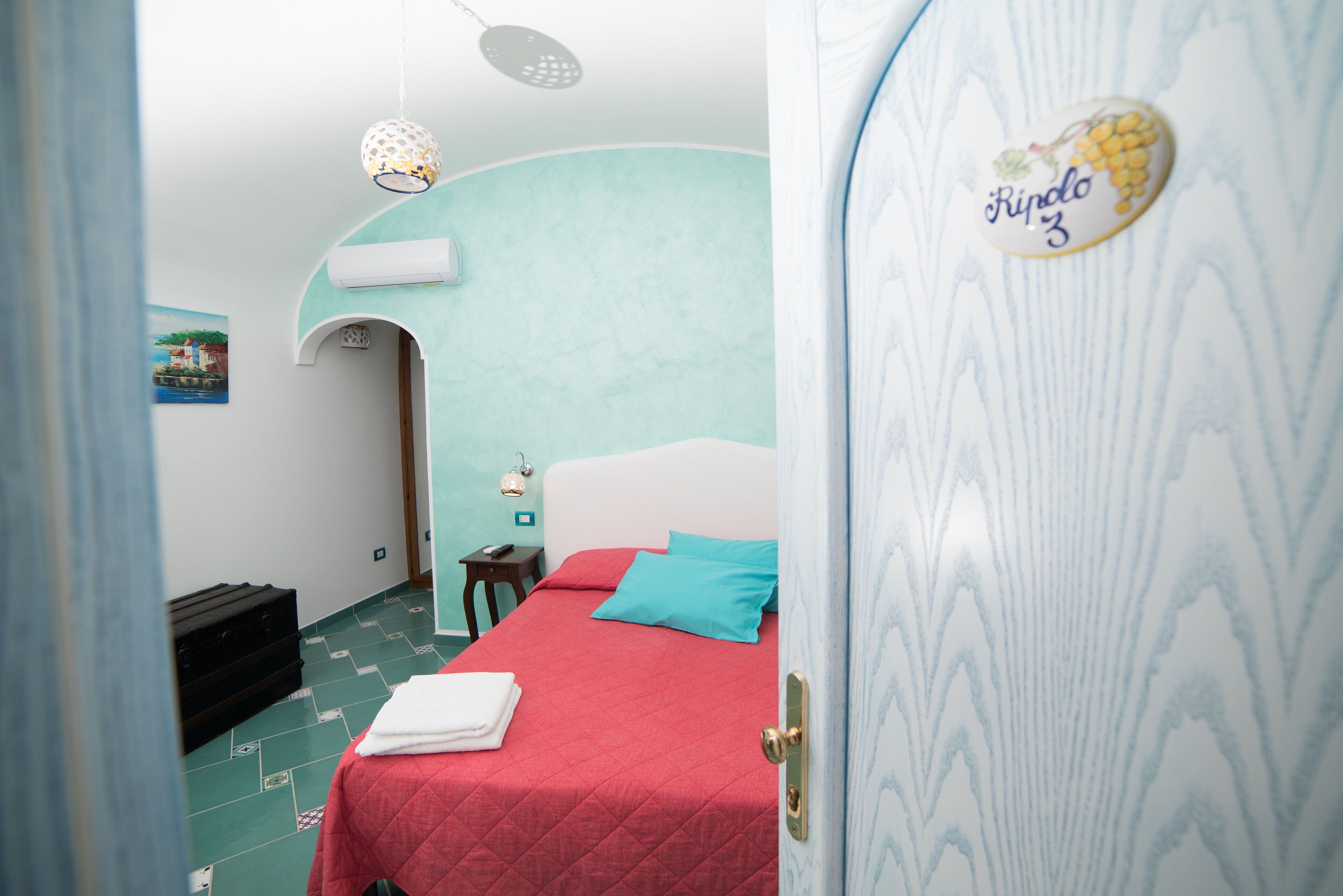 A room with a bed, a suitcase, a wall-mounted air conditioner, and a door with a sticker.