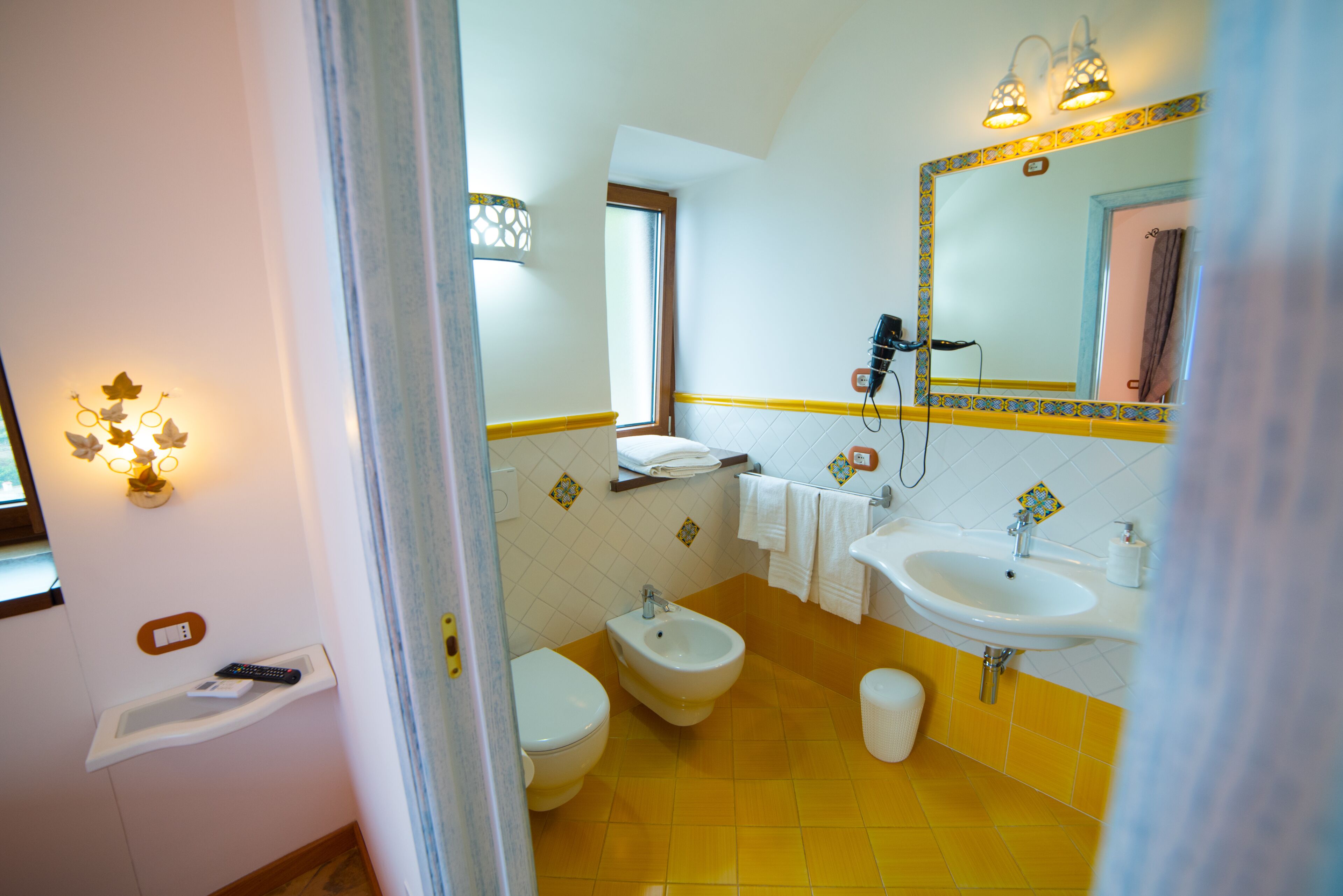 A bathroom with a bidet, toilet, sink, and a mirror with lights.