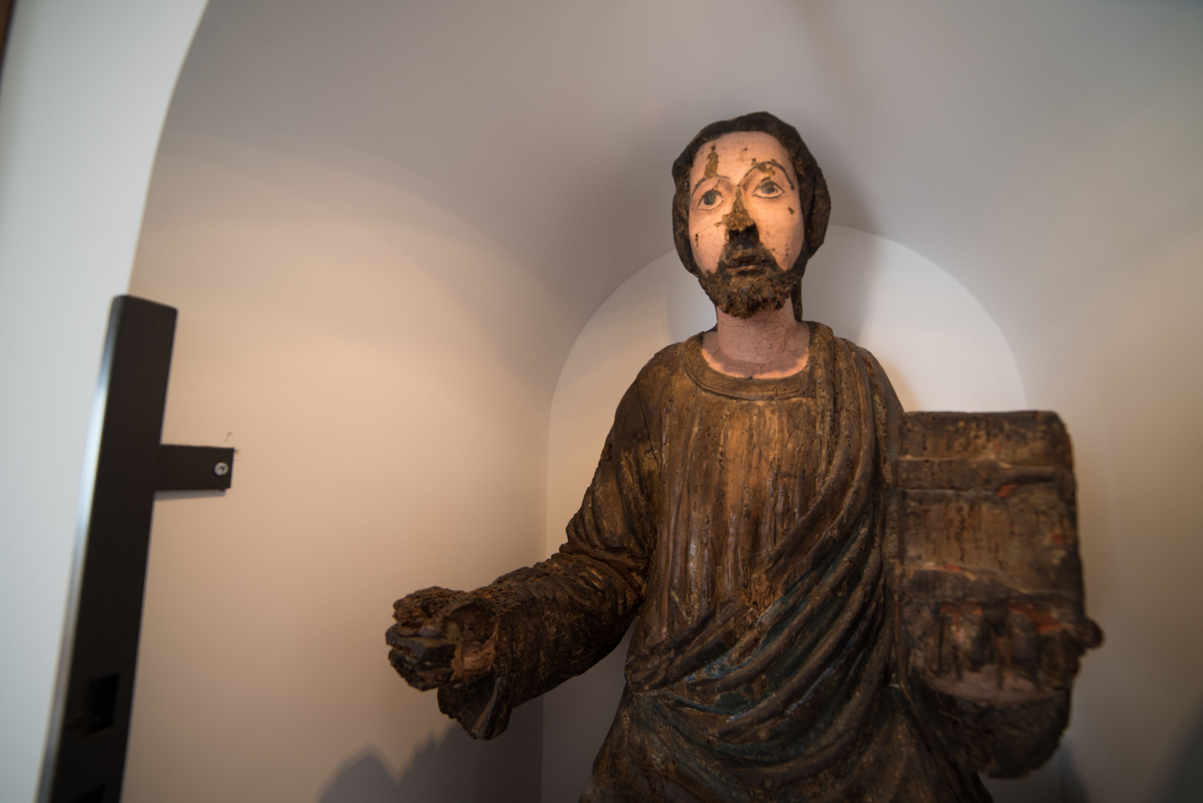 A statue with a cross on the wall behind it.