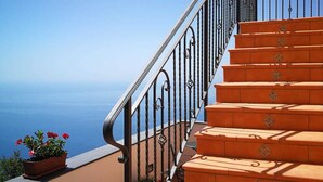 A staircase with orange steps and black railings, leading to a balcony with potted plants and a view of the sea. - San Giacomo Relais (Furore)