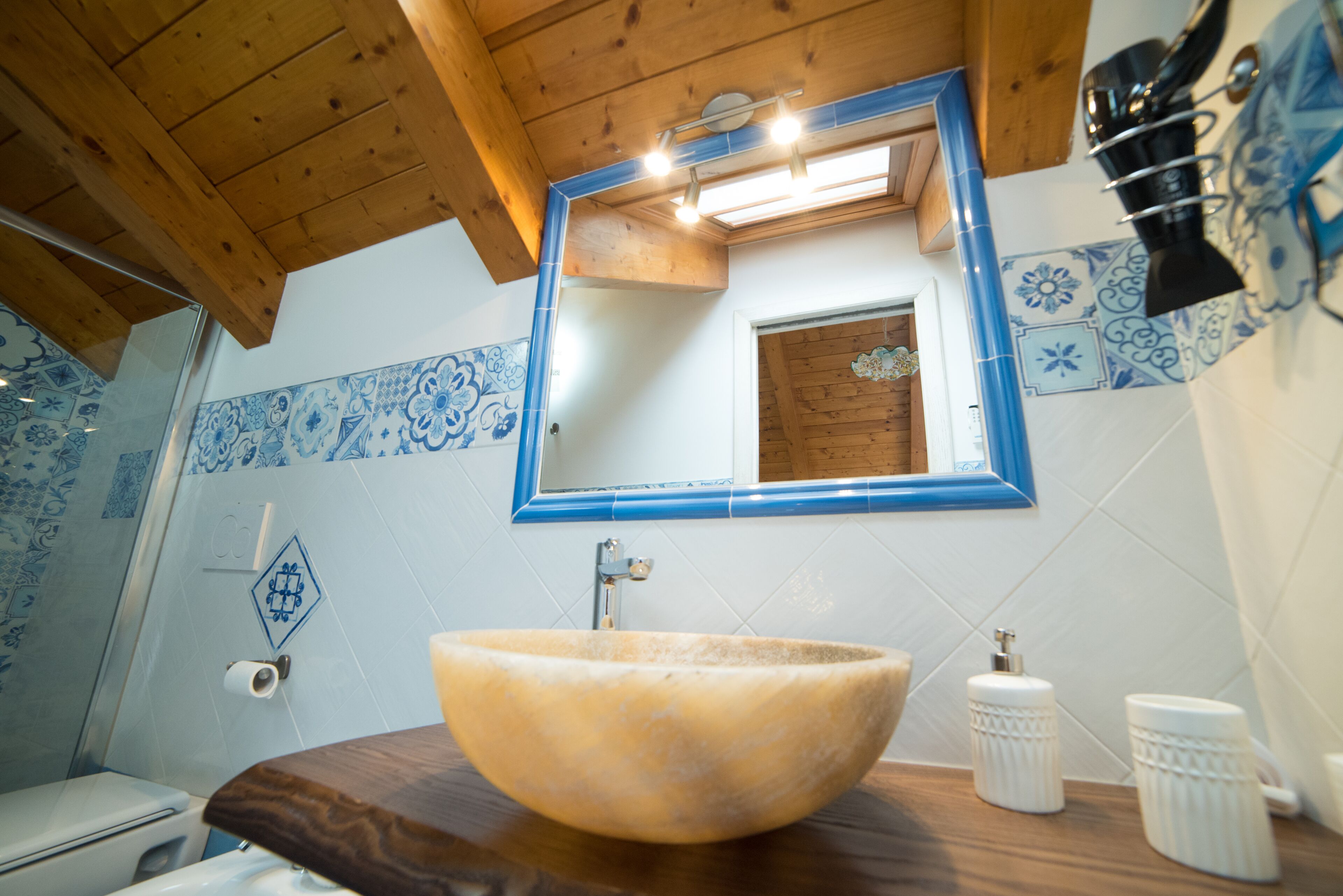 A bathroom with a wooden vanity, a large bowl sink, a mirror with a blue frame, and blue and white patterned tiles.