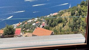 A view from a window overlooking a coastal area with a clear sky, a body of water, and a hillside with buildings. - San Giacomo Relais (Furore)