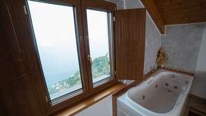 A bathroom with a bathtub, wooden cabinets, and a large window offering a view of the sea. - San Giacomo Relais (Furore)