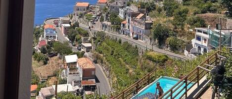 A coastal town with a view of the sea, a swimming pool, and a hillside with buildings.
