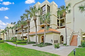 A multi-story hotel with balconies, palm trees, and a well-maintained lawn.
