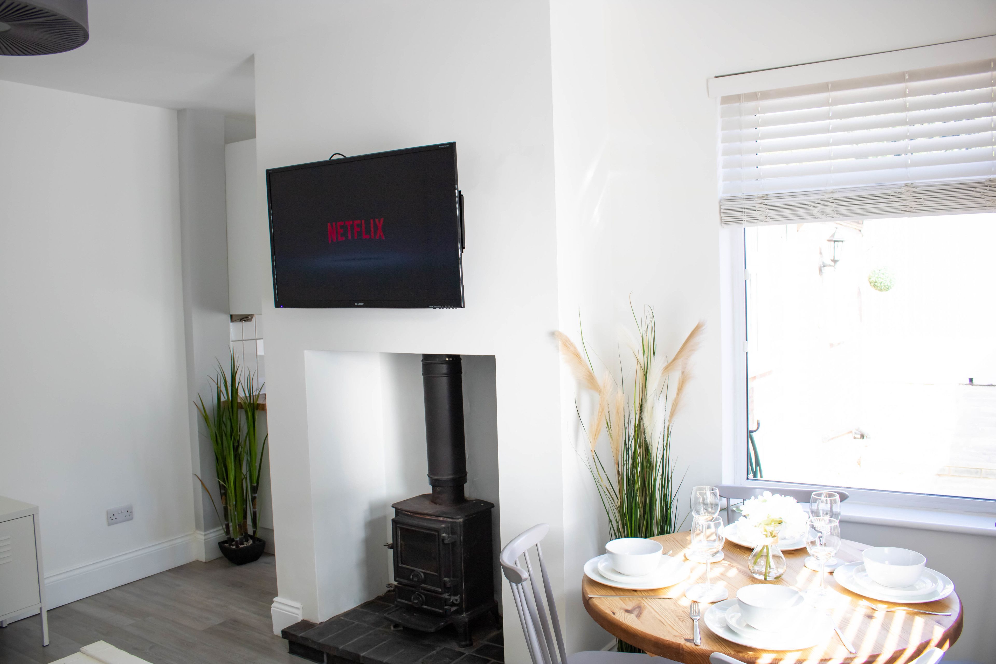 Ein modernes Wohnzimmer mit Kamin, einem Esstisch f ür vier Personen und einem an der Wand befestigten Fernseher.