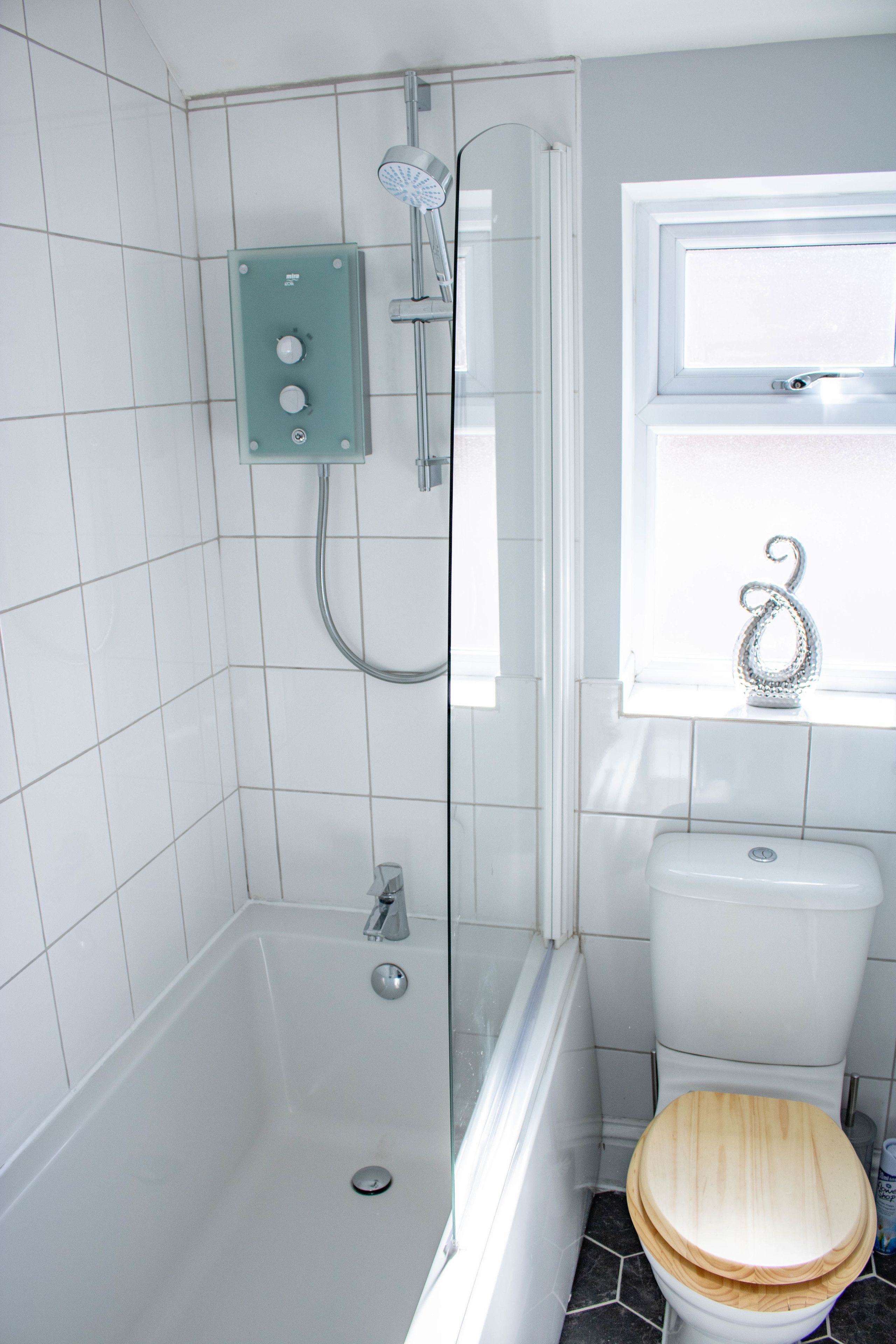 A bathroom with a shower, toilet, and window.