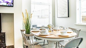 Comedor con una mesa redonda dispuesta para cuatro personas, sillas blancas y un jarrón con flores.