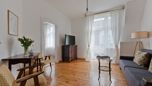 Een woonkamer met houten vloer, een bank, een televisie, een eettafel met stoelen en een lamp.