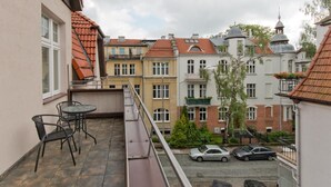 Een balkon met een tafel en stoelen, met uitzicht op een straat met geparkeerde auto's en gebouwen met rode dakpannen.