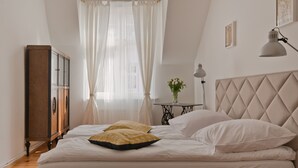 Een slaapkamer met een bed, nachtkastje, lamp en raam met dunne gordijnen.