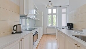 Een moderne keuken met witte kastjes, een waterkoker, een koffiezetapparaat en een raam dat voor natuurlijk licht zorgt.
