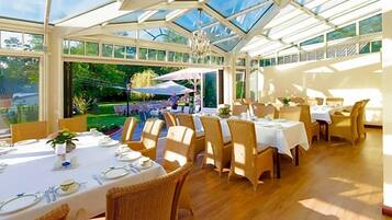 Ein Wintergarten mit gedeckten Tischen, Korbstühlen und einem Kronleuchter.