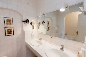A bathroom with two sinks, a large mirror, and framed pictures on the wall. - Tiemanns (Stemshorn)