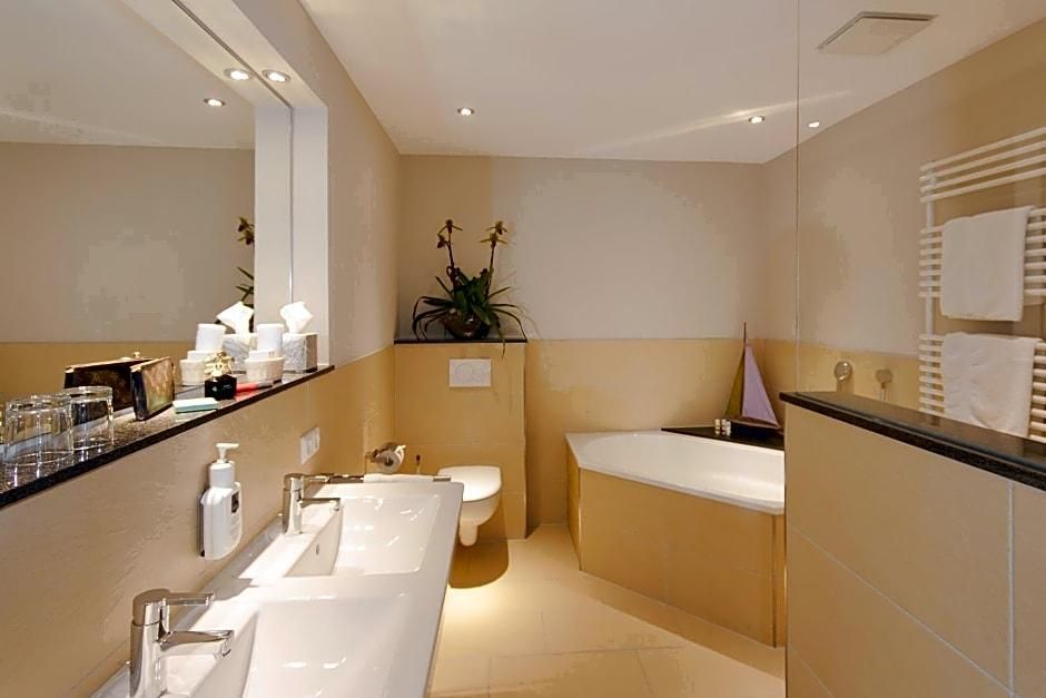 A modern bathroom with a large mirror, a bathtub, a toilet, and a sink.
