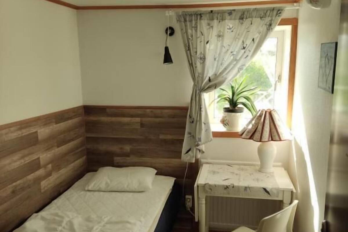 Ein kleines Zimmer mit einem Bett, einem Schreibtisch, einem Stuhl und einem fenster mit Vorhängen.