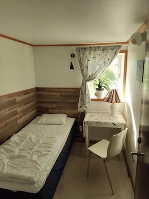 Une petite pièce comprenant un lit, un bureau, une chaise et une fenêtre avec des rideaux.
