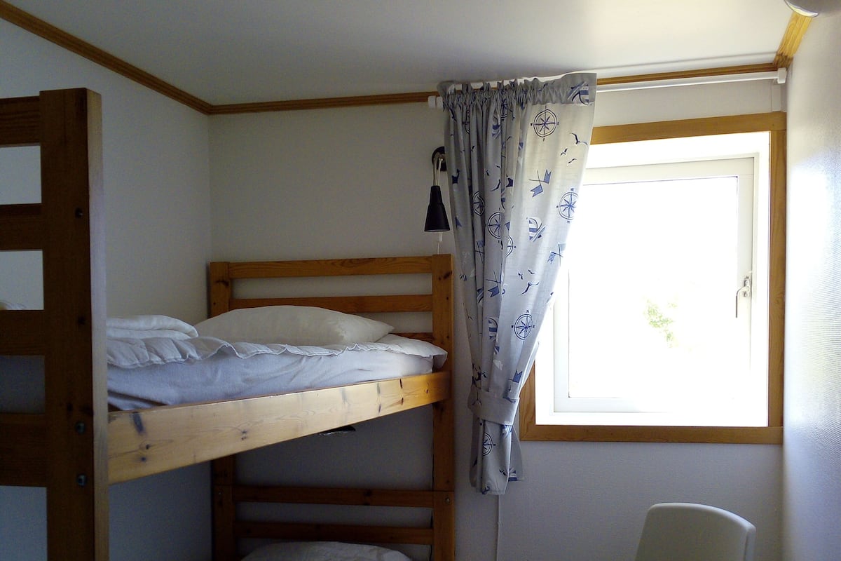 Ein Schlafsaalzimmer mit zwei Etagenbetten, einem Sessel, einem Fenster mit Vorhängen und einer Tür.