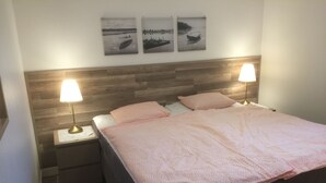 Ein ordentlich eingerichtetes Schlafzimmer mit einem Holz-Kopfteil, zwei Nachttischlampen, einem Bett mit rosa Bettwäsche und drei gerahmten Bildern an der Wand.