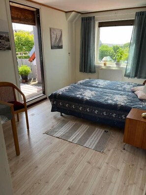 Une chambre à coucher avec un lit, une chaise, une fenêtre avec des rideaux et une vue sur la verdure à l’extérieur.