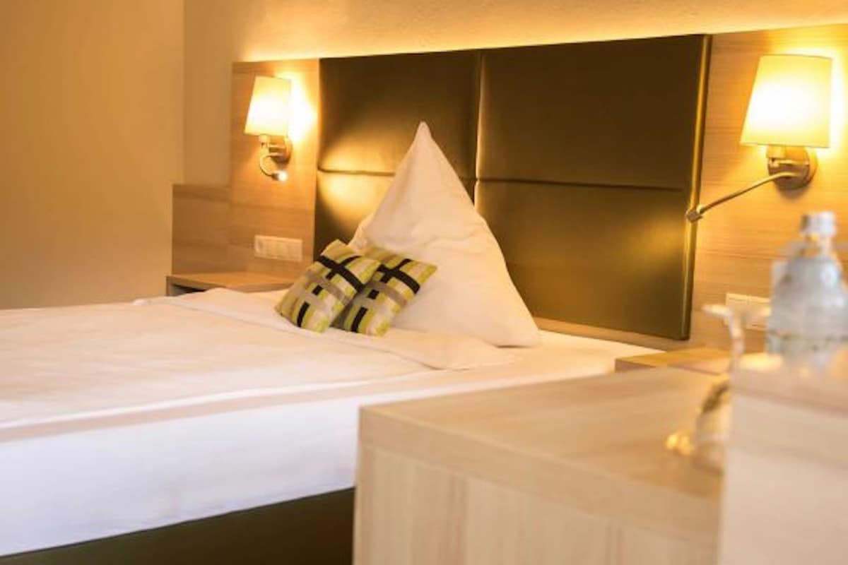 Une chambre d’hôtel avec un lit, une table de chevet et deux lampes fixées au mur.
